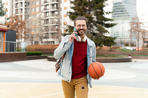 Portrait of a young man cooling down after playing basketball and talking on mobile phone