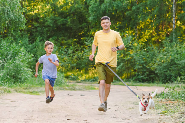 pai e filho correndo pela estrada de terra do país com cachorro na coleira da cintura - men jogging running sports training - fotografias e filmes do acervo