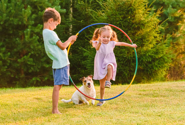 フラフープを飛び越えるペットの犬と遊ぶ子供たち - playful ストックフォトと画像