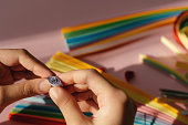 Paper and quilling tools on a pink background with hands and space for text and design.