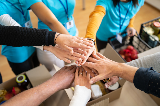A group of charity workers hands stacked into a circle for unity, over boxes of groceries