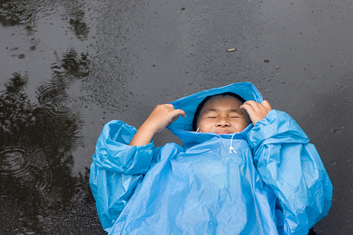 Little boy in rain playing in raincoat outdoors