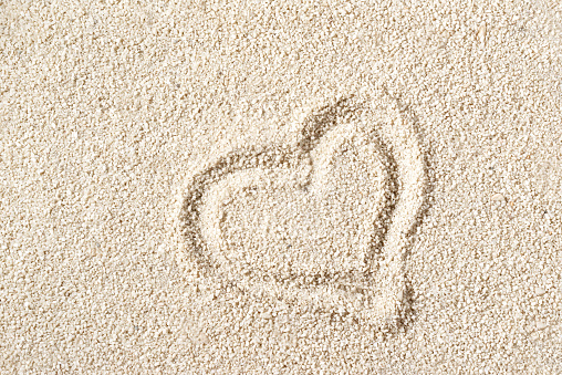 Romantic summer vacation concept, happy love honeymoon travel, heart shape symbol on a beach sand beige texture, minimalist aesthetic background
