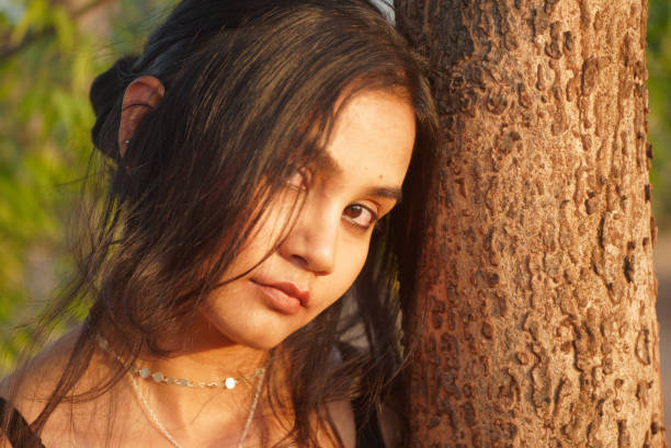Indian Asian young female close up portraits of emotion facial gesture mood feeling in outdoors daylight leaning next to a tree stock photo