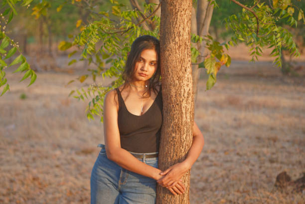 Indian Asian young female close up portraits of emotion facial gesture mood feeling in outdoors daylight leaning next to a neem tree stock photo