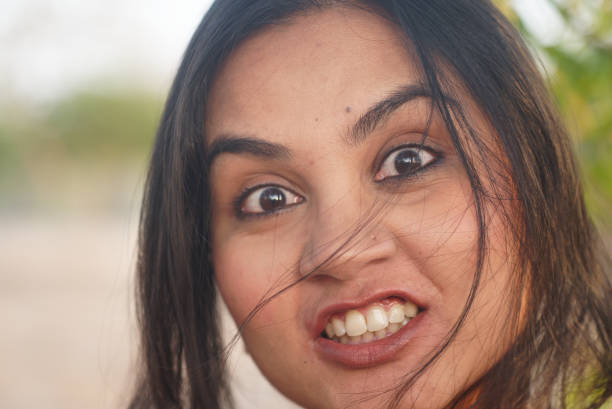 Indian Asian young female close up portrait of some anger clenching teeth emotion looking into camera facial gesture mood feeling in outdoors daylight stock photo