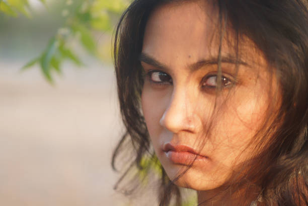 Beautiful Indian Asian young female macro close up portrait of emotional vulnerability anger soft mood staring away from the camera in a side ways glance with hair falling over her cheeks stock photo
