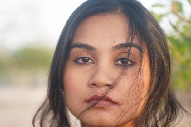 Asian Indian female close up portrait of serious neutral emotion looking into camera in outdoors evening light stock photo