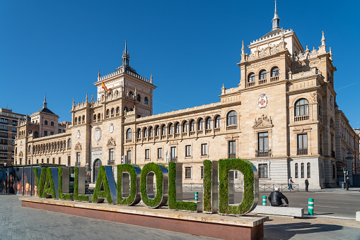 Valladolid, Spain - November 12 2022: Cavalry Academy building in the center of Valladolid, In front is written the name of the city written decorated with grass an flowers. Plaza de Zorrilla Square