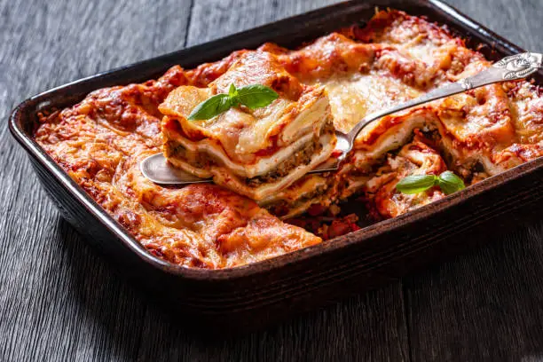 Lasagna with ricotta cheese, ground beef, mushrooms, and tomato sauce in baking dish with cake shovel, landscape view