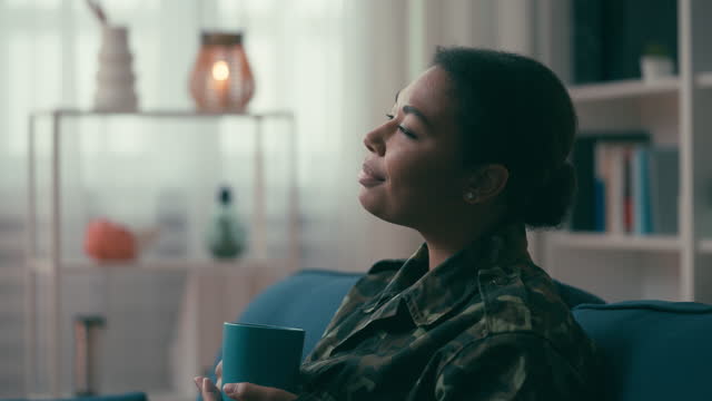 Relaxed military woman inhaling coffee cup aroma, enjoying home comfort on couch