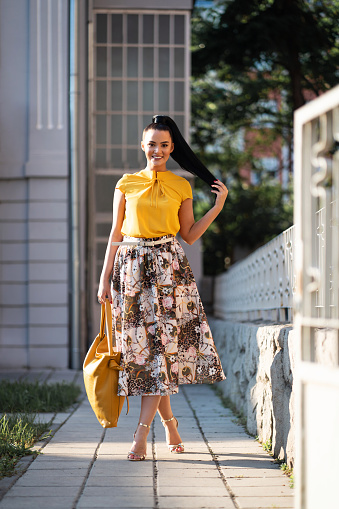 Portrait of a charming young Caucasian woman in yellow shirt, floral skirt, and yellow bag