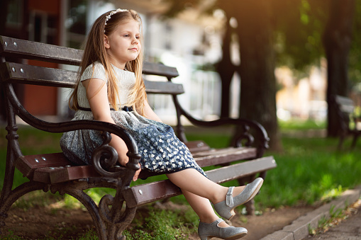 Cute Caucasian girl in a dress sitting on the bench