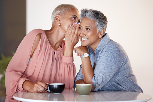 Senior women, bonding or whispering secrets in coffee shop, restaurant or cafe and funny gossip, news or story. Smile, happy or retirement elderly friends whispering in ear or sharing in rumor spread