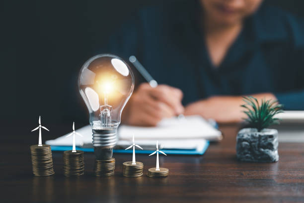 istock Businesswoman with lightbulb on coins and using calculator to calculate and money stack. Save energy and money with accounting finance in office concept. Idea of energy saving planning in home. 1477745957