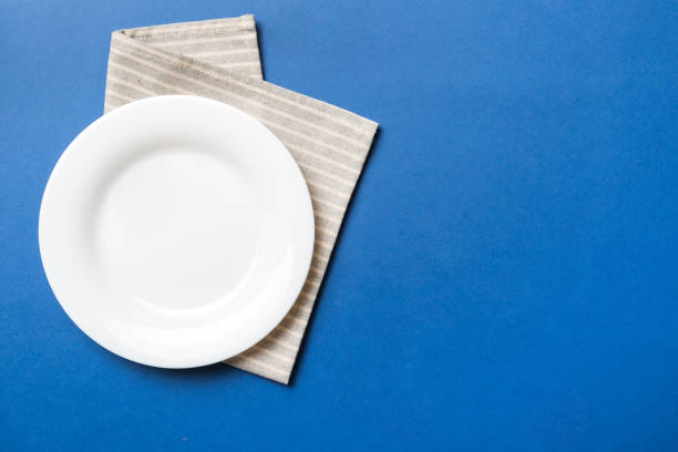 istock Top view on colored background empty round white plate on tablecloth for food. Empty dish on napkin with space for your design 1477751750