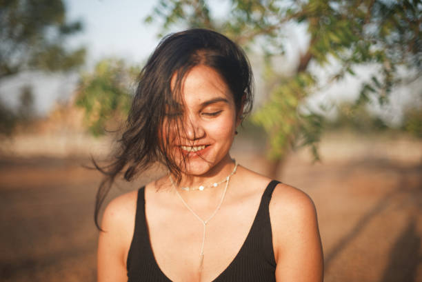 Indian Asian young female close up portraits of emotion facial gesture of gentle shy laughter with hair falling over her face  in outdoors daylight stock photo