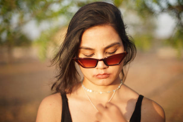 Indian Asian young female close up portraits of emotion facial gesture mood looking down with sunglasses lowered feeling in outdoors daylight stock photo