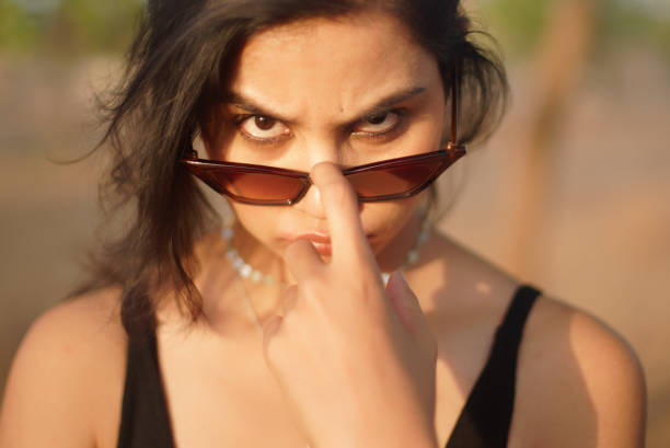 Indian Asian young female close up portrait of questioning serious emotion while pulling down sunglasses face eyes mood feeling in outdoors daylight stock photo