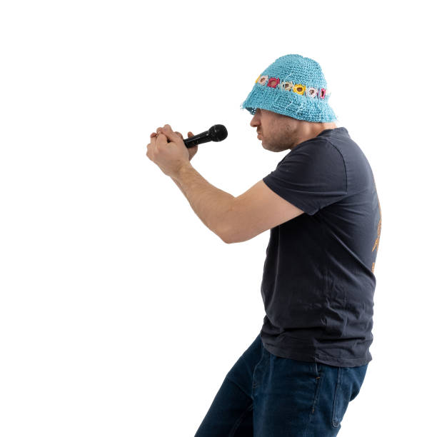 istock A funny mature man in a bright hat holds a microphone in his hands. Isolated on a white background. 1477756843