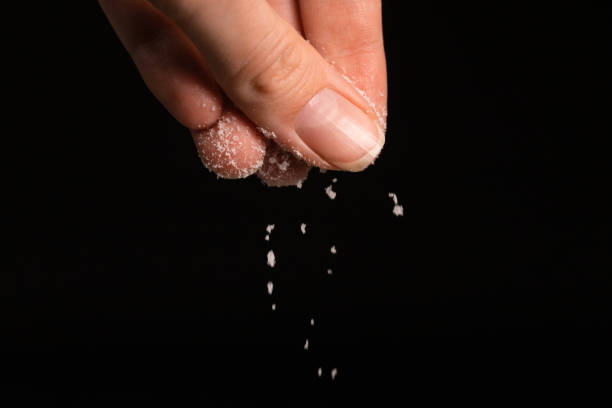 istock Female fingers sprinkle salt on a black background, copy the space. Macrophotography 1477761005