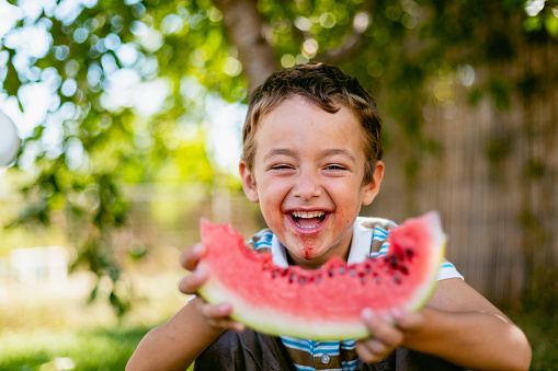 Smiling messy boy eating slice of watermelon on hot summer day