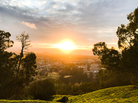 Sun setting over the city of Berkeley, California on a hill. It was a cloudy day with the sun slipping through a crack within the cloud layers.