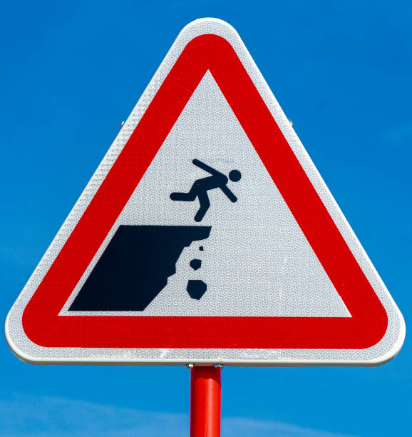 istock Triangular road sign of danger of person falling on cliff under blue sky background. 1477765732