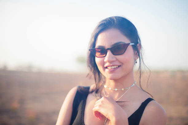 Indian Asian young female close up portrait of happy emotion facial gesture mood feeling in outdoors daylight wearing sunglasses stock photo