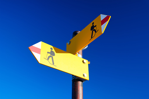 Hiking and traveling in the mountains. Directional marker for a mountain hike. Yellow bright sign with an arrow against the blue sky. Navigation in a hiking trip.