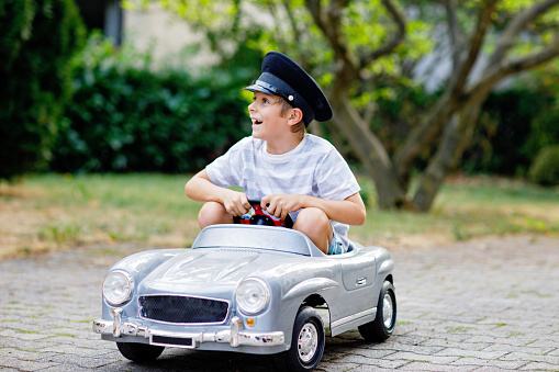 Happy kid boy playing with big old toy car in summer garden, outdoors. Healthy child driving old vintage car taxi. Laughing and smiling kid. Family, childhood, lifestyle concept.