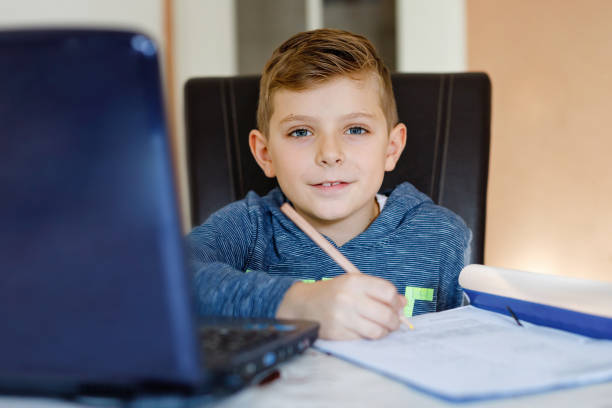 istock Happy healthy kid boy with glasses making school homework at home with notebook. Interested child writing essay with helping of internet. concetrated schoolchildren concept 1477773007