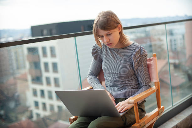 istock Young girl sitting director's chair using laptop while on balcony 1477773551