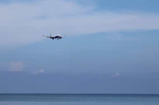 A passenger plane is flying in the blue sky over the ocean