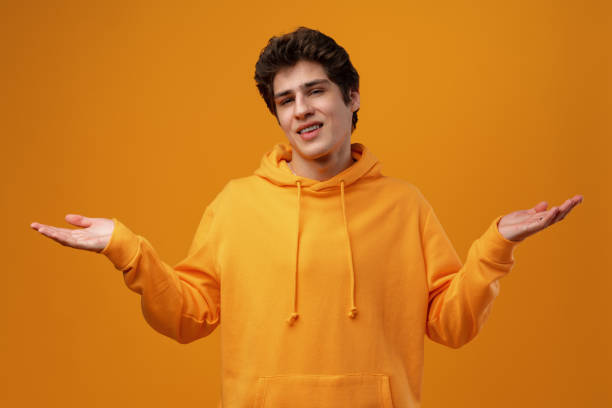 young man standing over yellow background clueless and confused with open arms - blank expression head and shoulders horizontal studio shot imagens e fotografias de stock