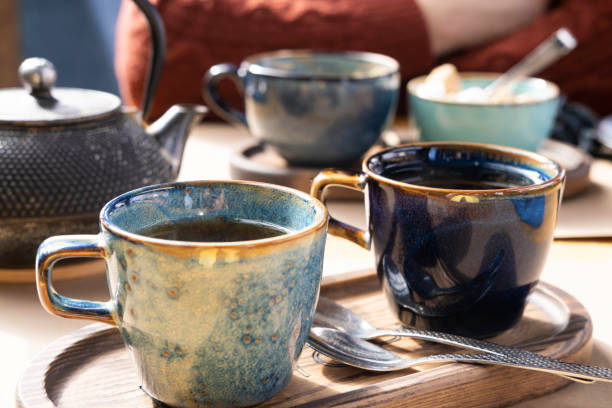 Brewing and Serving Tea. Beautiful Teapot Pouring Green Tea in Blue Ceramic Cup on Wooden Cafe Table. Two Pottery Handmade Mugs Early in the Morning. Trendy Authentic Porcelain Set. Breakfast Concept. Tea Time. Trend of stylish Dishware, Tableware. High tea preparar y servir té. tetera vertiendo té verde en taza de cerámica azul sobre mesa de café de madera. dos tazas de cerámica hechas a mano temprano en la mañana. moderno conjunto de porcelana auténtica. concepto de desayuno. hora del té.