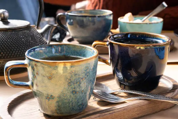 Brewing and Serving Tea. Beautiful Teapot Pouring Green Tea in Blue Ceramic Cup on Wooden Cafe Table. Two Pottery Handmade Mugs Early in the Morning. Trendy Authentic Porcelain Set. Breakfast Concept. Tea Time. Trend of stylish Dishware, Tableware. High tea