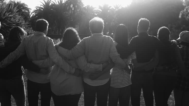 Crowd of multigenerational people hugging each other in front of camera - Multiracial friends with different ages having fun together at city park