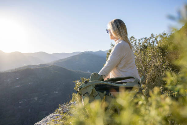 istock Mature female hiker relaxes at summit viewpoint above distant mountains 1477786351