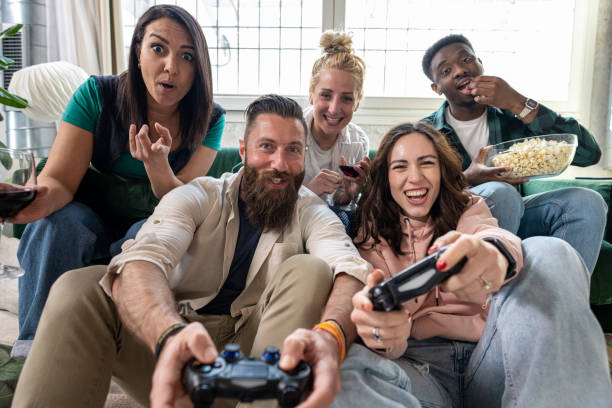 Overjoyed young friends playing video games at home, multiracial group of people having fun during lazy and relaxed weekend