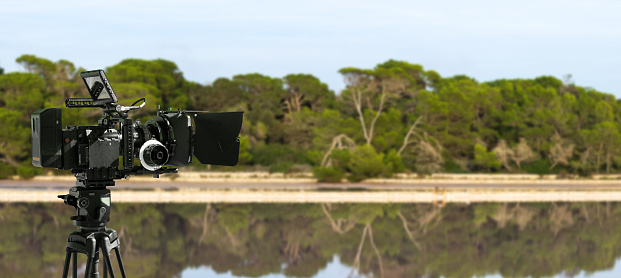 Digital movie camera making film in nature. 
a video camera films an outdoor shot near a lake and a forest. Wide background with copy space for documentary production.
