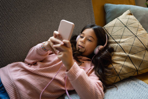 istock Schoolgirl lying on the sofa, listen to music while using mobile phone 1477792375