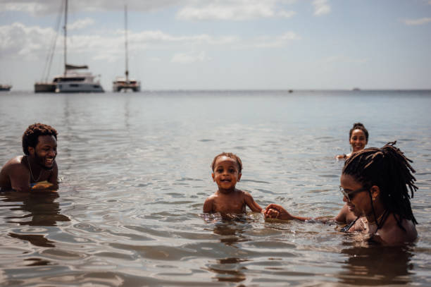 Shot of a boy wearing swimwear and smiling knee deep in water, sky and volcanic rocks behind. Taken in Kauai, Hawaii, during the day.
