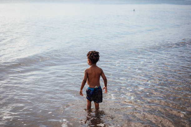Cute little boy playing with a rock on the beach by the sea in sunset.