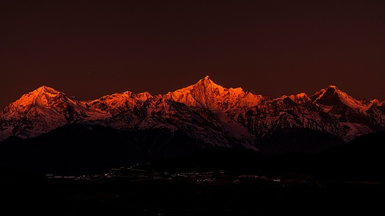 An awe-inspiring nightscape featuring a vibrant red sky draped over cold Meili Snow Mountain in Tibet