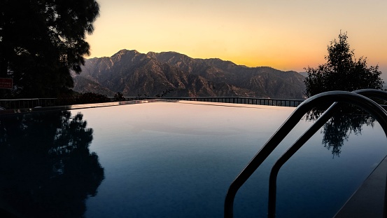 A vibrant outdoor shot of an infinity pool, surrounded by mountains and illuminated by a vivid sunset