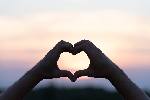 Adult male making a gesture with his hands in a heart shape on a sunset background