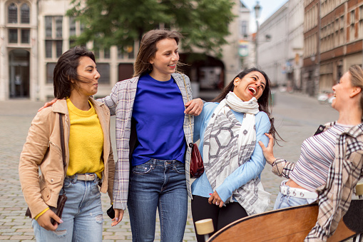 four young women friends laugh carefree in the city center - focus on Indian woman face on the right