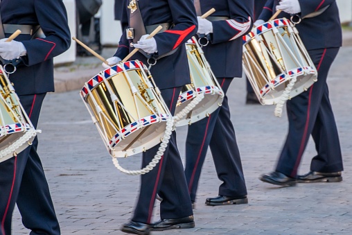 A close up of a group of uniformed drummers marching in unison down a city street, playing their drums