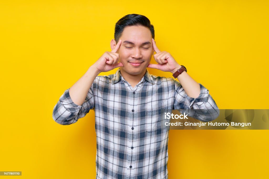Portrait of pensive Young Asian man in plaid shirt close eyes and trying hard to remember something isolated on yellow background. people lifestyle concept Contemplation Stock Photo